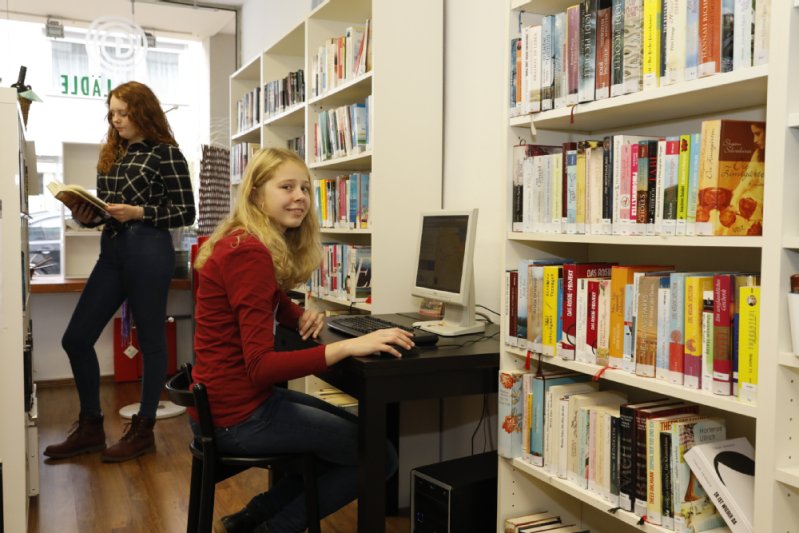 Zwei Mädchen vor Bücherregalen und einem PC